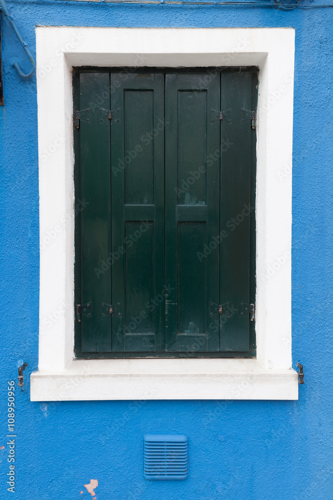 Old window with dark green shutters on blue wall Old window with dark green shutters on blue wall
