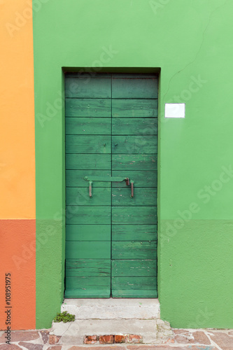 Old wooden green locked door with peeling paint in the green wal © arturko