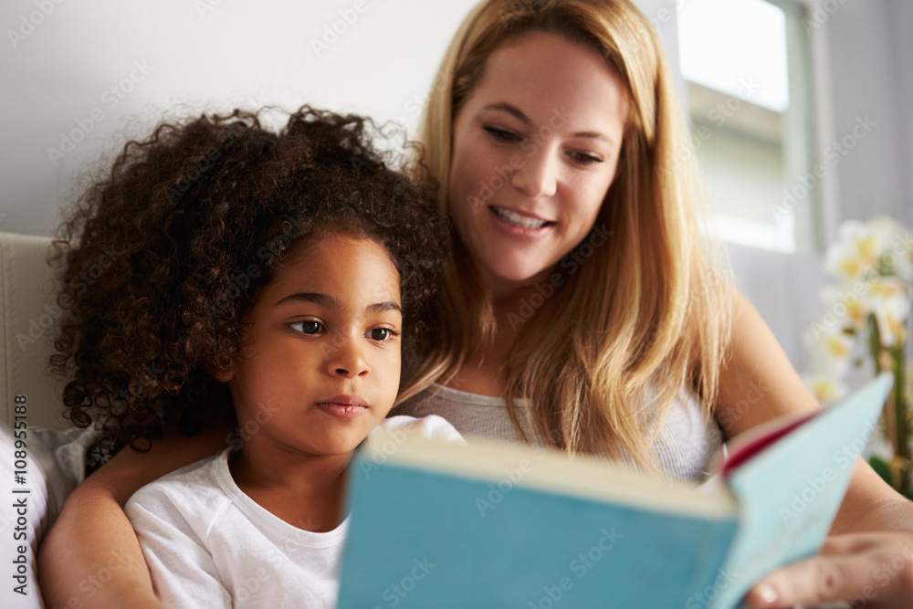 Caucasian mum and black daughter read book in bed, close-up Caucasian mum and black daughter read book in bed, close-up