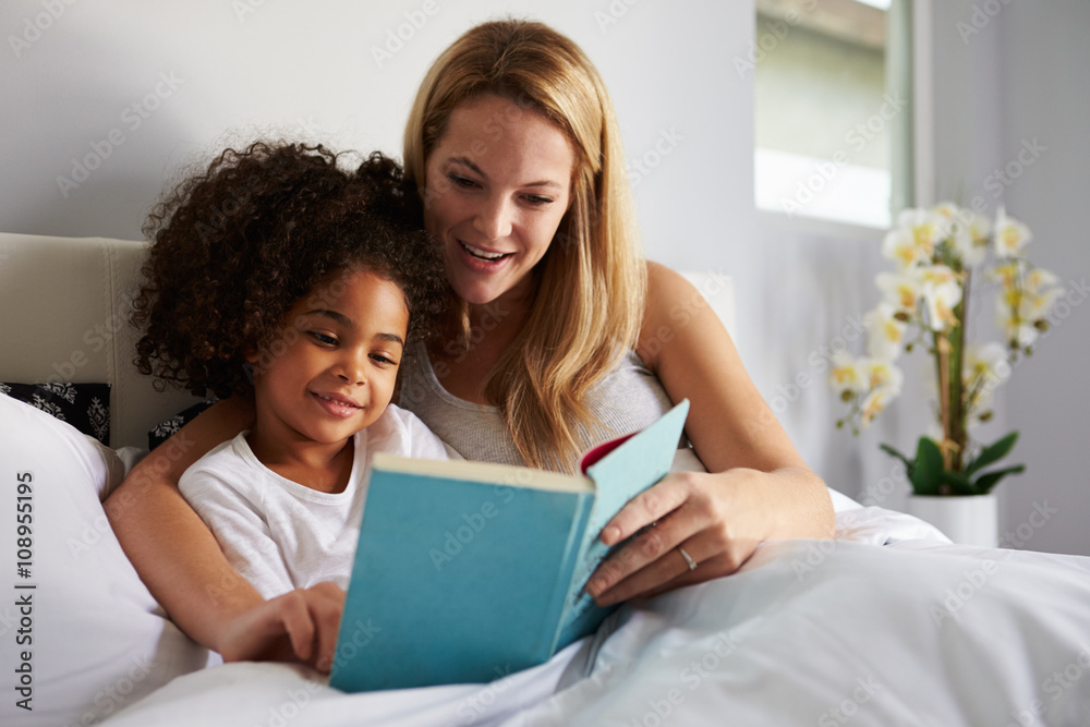 Caucasian mum and black daughter read a book together in bed Caucasian mum and black daughter read a book together in bed