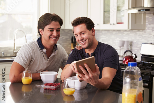 Male gay couple looking at tablet computer over breakfast