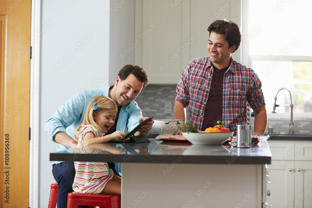 Girl using tablet computer in kitchen with her male parents Girl using tablet computer in kitchen with her male parents
