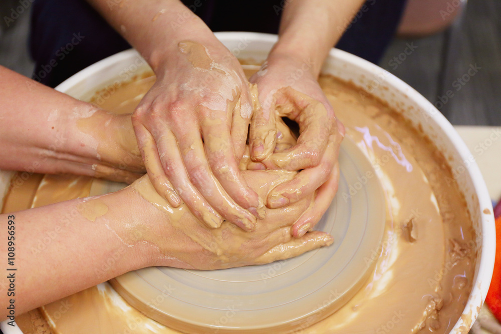 woman potter helps student how to hold hands in the manufacture of the vessel on the potter's wheel