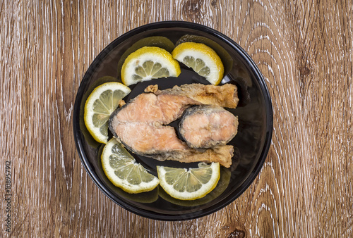 Fried fish ( with sliced lemon ) in a plate on wooden background