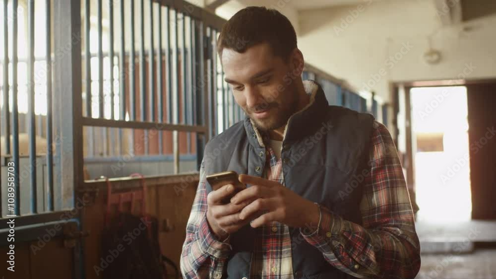 Happy smiling man is using a smartphone next to a horse in a stable. Shot on RED Cinema Camera.