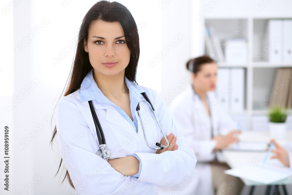 Brunette female doctor on the background of colleagues talking to each other in hospital Brunette female doctor on the background of colleagues talking to each other in hospital