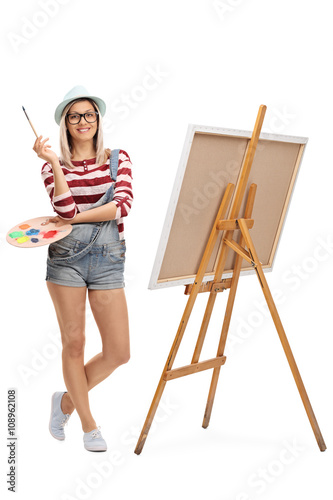 Woman posing with a paintbrush by an easel