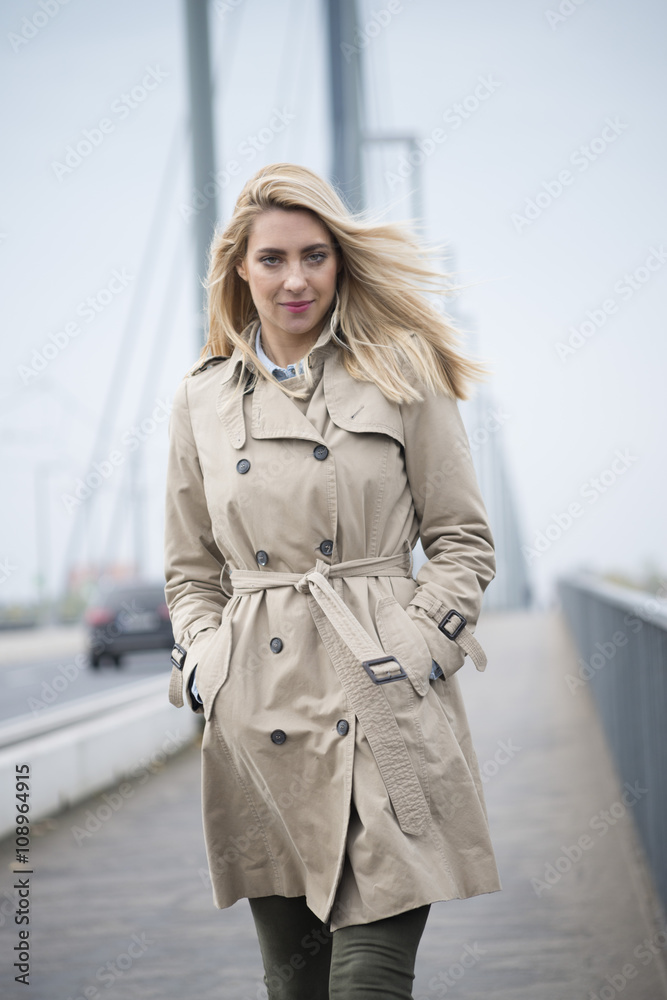 Portrait of young woman wearing trench coat walking on a bridge Portrait of young woman wearing trench coat walking on a bridge