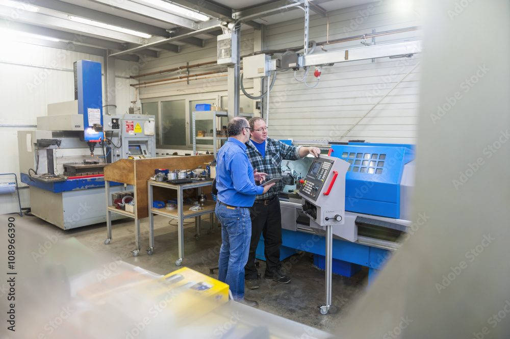 Two men in factory talking at machine for mold making Two men in factory talking at machine for mold making