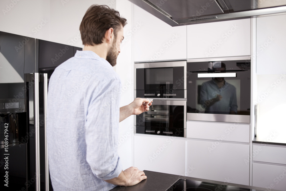 Man standing in his built-in kitchen switch on the oven with remote control Man standing in his built-in kitchen switch on the oven with remote control