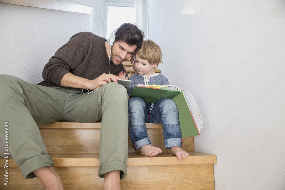 Father and son sitting on stairs, reading book and listening music Father and son sitting on stairs, reading book and listening music