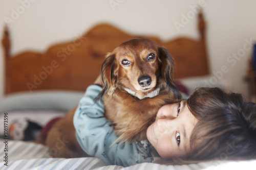 Smiling little boy lying on bed with long-haired Dachshund photo