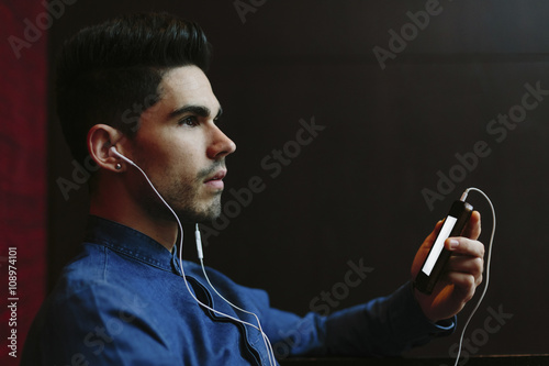 Profile of young man hearing music with earphones in front of black background photo