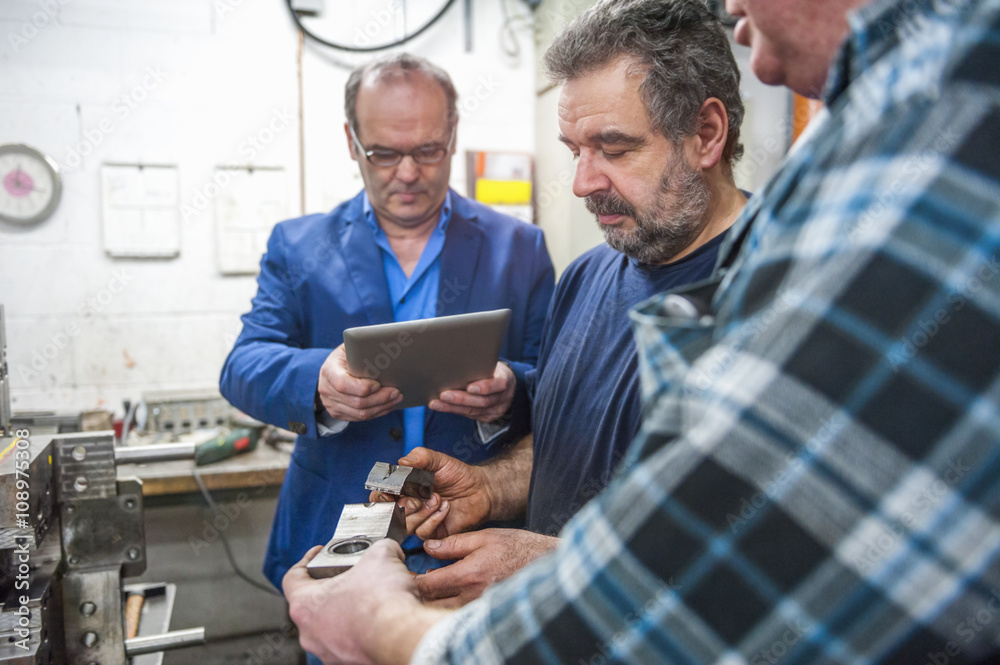 Three men with digital tablet examining workpieces Three men with digital tablet examining workpieces