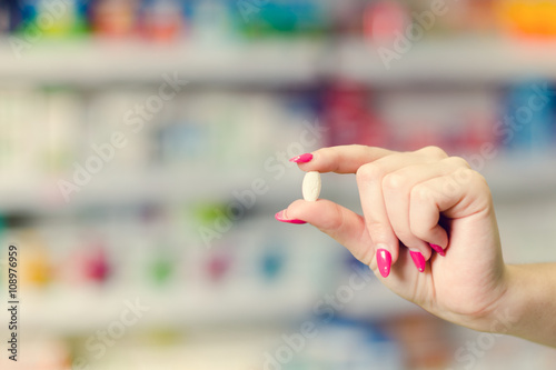 Woman hand hold a pill. Pharmacy drugstore is background. 
