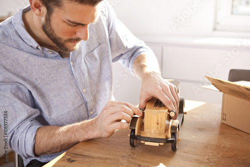 Young man sitting at table with wooden toy car photo