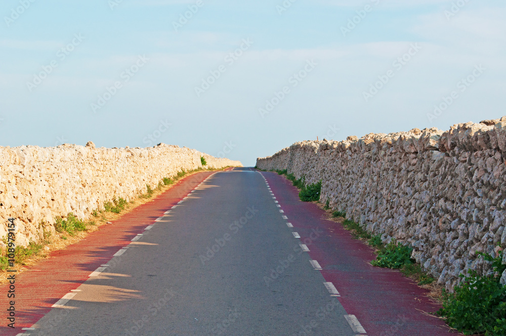 Minorca, Isole Baleari, Spagna: la strada rossa e i muretti di pietra verso il faro di Punta Nati il 12 luglio 2013