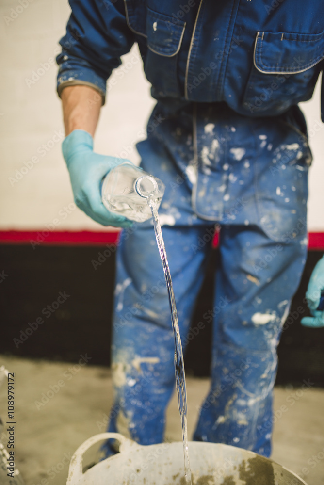 Bricklayer preparing cement in bucket, pouring water from bottle Bricklayer preparing cement in bucket, pouring water from bottle