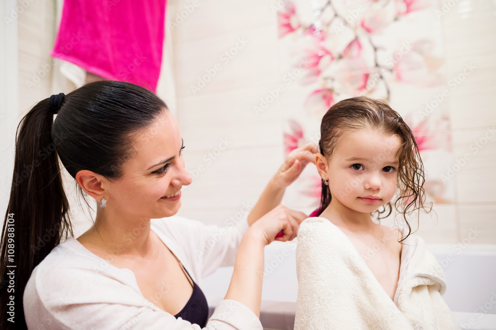 Mother combing hair of her daughter after taking bath