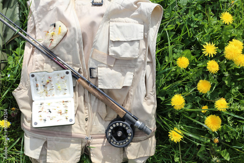 Un gilet ,une canne et son moulinet avec une boite de mouche artificielles pour la pêche posé par terre dans un champs photo