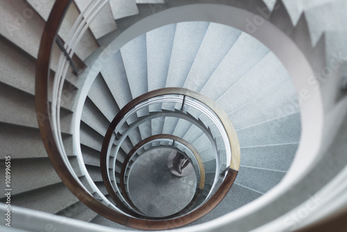 Fotografie White spiral staircase in soft light with wooden banister looking down from above