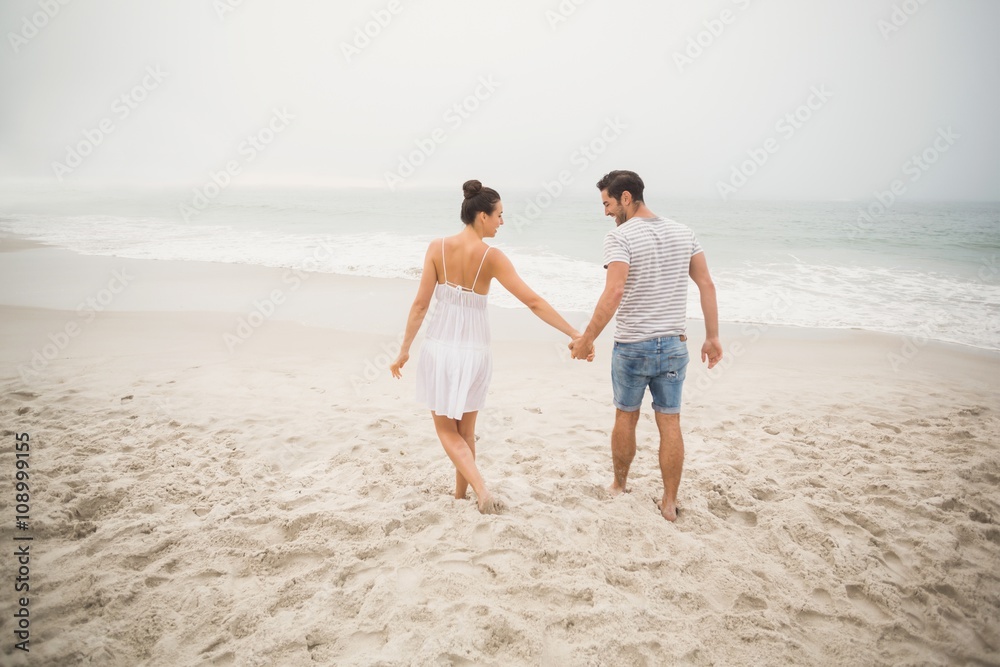 Rear view of couple holding hands and walking on the beach