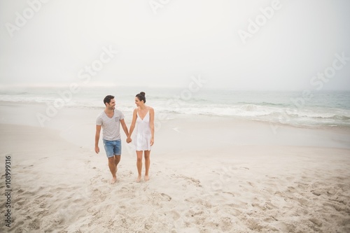 Happy couple holding hands and walking on the beach
