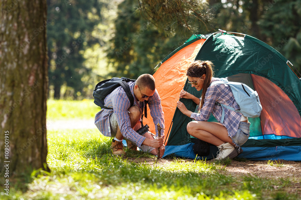Young campers setting up the tent at the forest. - obrazy, fototapety, plakaty 