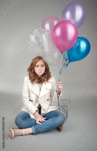 Sad young adult sitting on floor holding balloons