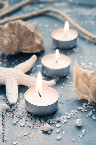 Three burning candles in a row on background of sea objects, tin