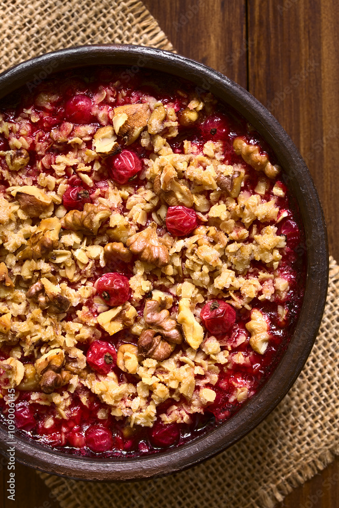 Redcurrant crumble or crisp with oatmeal and walnut on top baked in rustic bowl, photographed overhead on dark wood with natural light (Selective Focus, Focus on the top of the crumble)