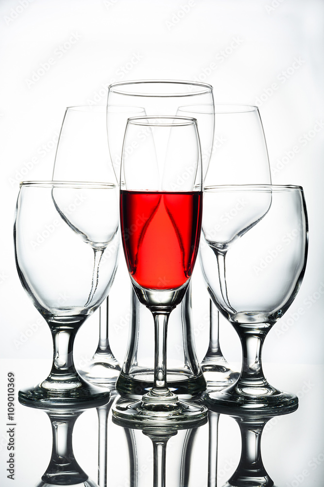 Red water in wine glass and empty glasses on white background