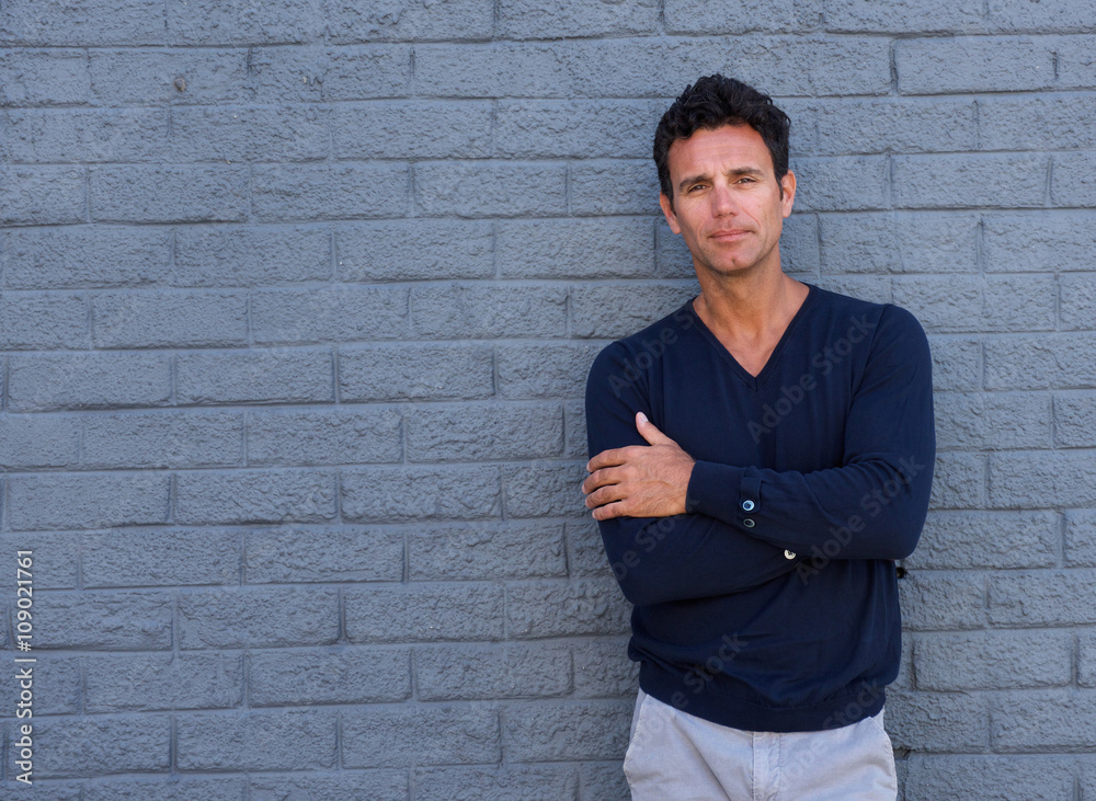 Mature man standing against gray wall with arms crossed Mature man standing against gray wall with arms crossed