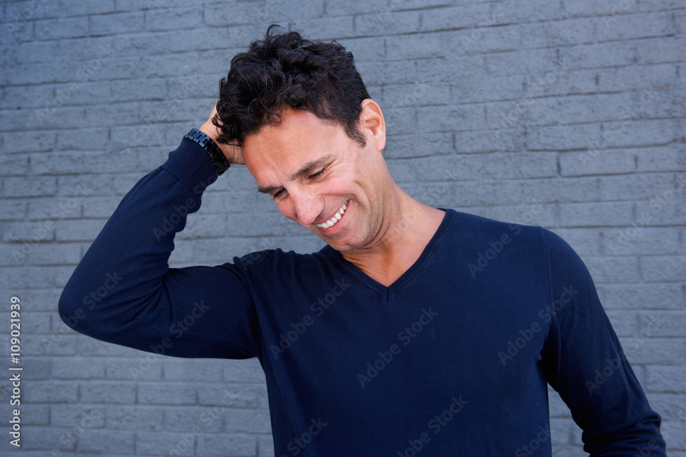 Handsome man laughing with hand in hair against gray wall Handsome man laughing with hand in hair against gray wall