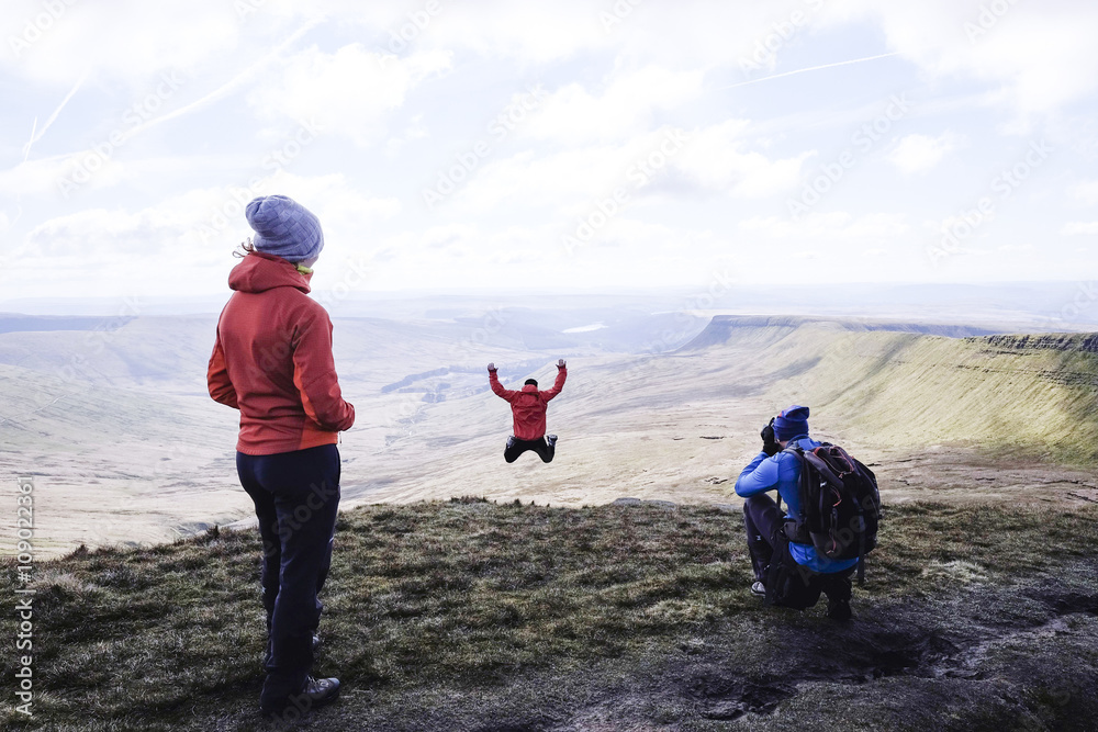 A group on top of a mountain, with a photographer and a girl jumping, Pen Y Fan - obrazy, fototapety, plakaty 