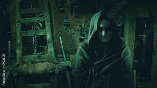 Medieval inquisitor in the hood on the inquisitors tools backgro