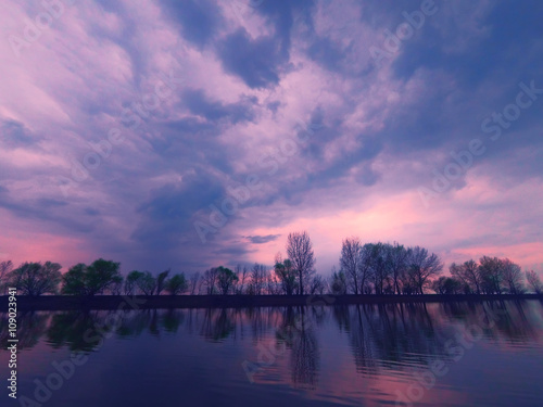 Picturesque view of the river with reflections of the trees on far riverbank. Dramatic evening scene under stormy rainy clouds. Volga-river near Astrakhan  Russia