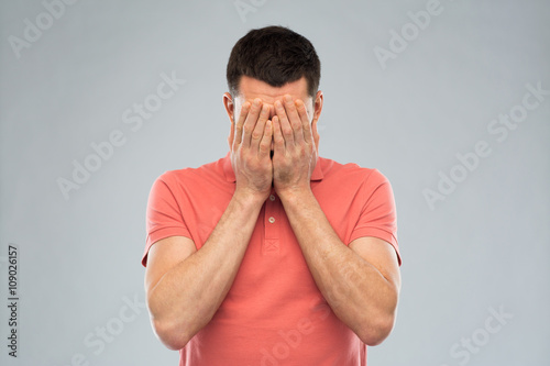 man in t-shirt covering his face with hands