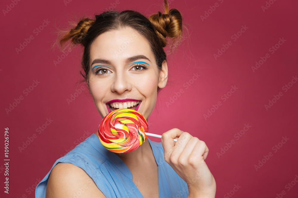 Closeup of beautiful smiling young woman biting colorful lollipop