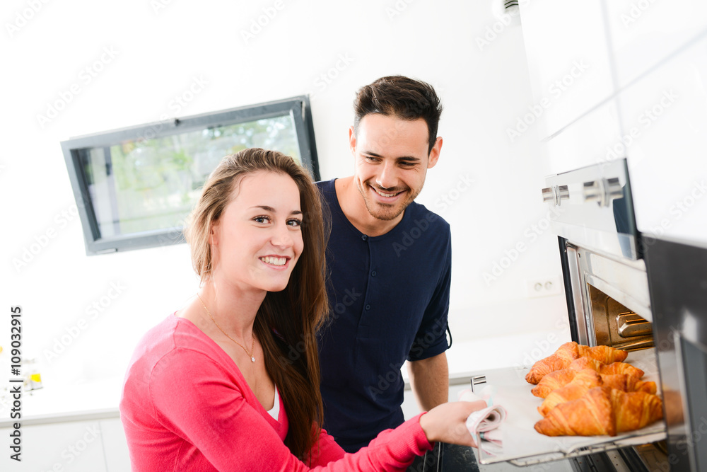 cheerful young woman taking out of oven just baked homemade croissant