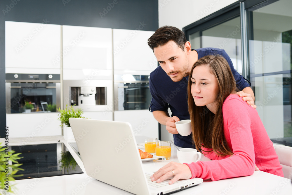 young couple at home having coffee in kitchen and working on laptop computer young couple at home having coffee in kitchen and working on laptop computer