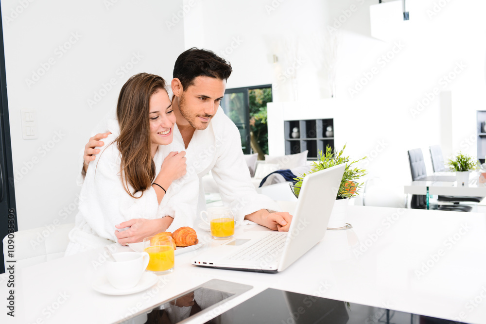 young couple in bathrobe at home having coffee in the kitchen and working on laptop computer young couple in bathrobe at home having coffee in the kitchen and working on laptop computer