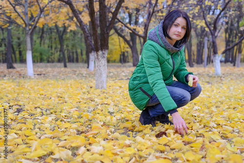 Serious young woman kneeling among fallen leaves