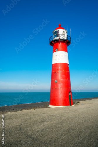 Red and white lighthouse against a bright blue sky