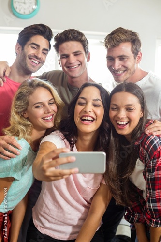 Happy friends smiling while taking selfie at home