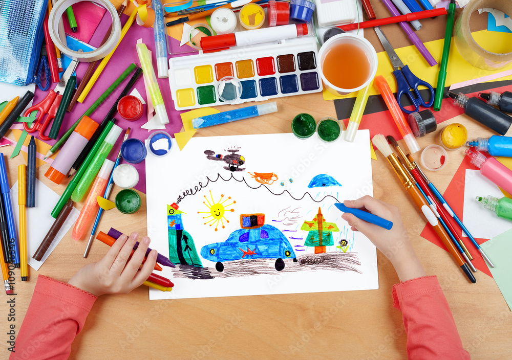 Obraz premium child drawing police car and helicopter, top view hands with pencil painting picture on paper, artwork workplace