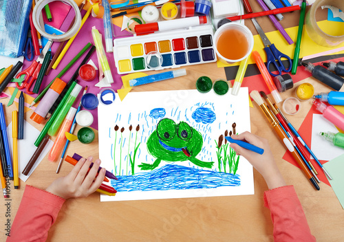 child drawing frog in river, top view hands with pencil painting picture on paper, artwork workplace