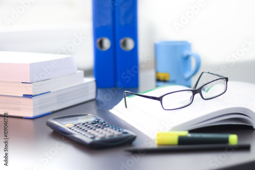 Schreibtisch / Arbeitsplatz mit Büchern, Brille, Taschenrechner und Ordnern