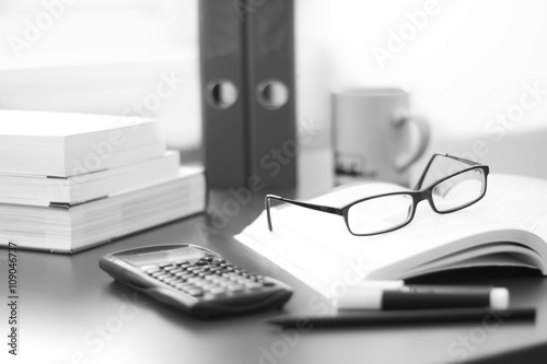 Schreibtisch / Arbeitsplatz mit Büchern, Brille, Taschenrechner und Ordnern, schwarz weiß