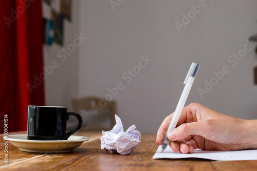 Hand holding and writing a pen. Coffee at a wooden table. Selective focus.